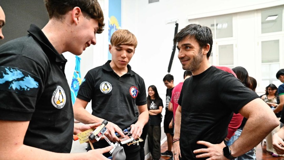 Torres conversando con dos estudiantes que participaron de la Liga de Robótica. la 