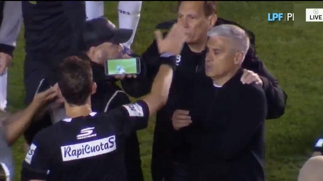 El cuerpo técnico del All Boys saca un celular para mostrárselo al árbitro y demostrar que no fue penal.